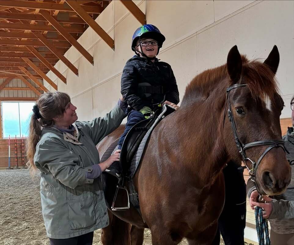 Children smiling on horses with an instructor during an adaptive riding session